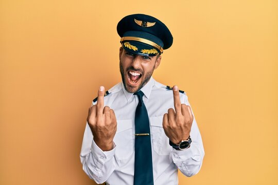 Handsome Hispanic Man Wearing Airplane Pilot Uniform Showing Middle Finger Doing Fuck You Bad Expression, Provocation And Rude Attitude. Screaming Excited