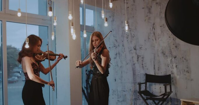 Beautiful duet of admiring women playing the violins at window indoor