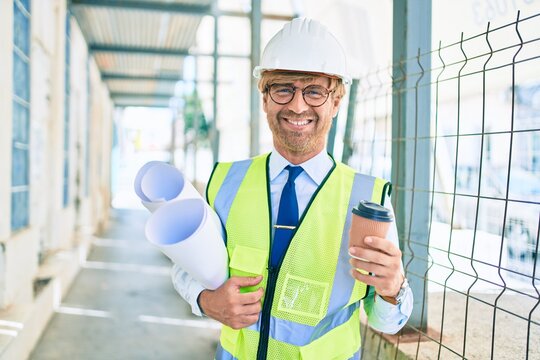 Business architect man wearing hardhat standing outdoors of a building project wearing reflective vest drinking a cup of coffee