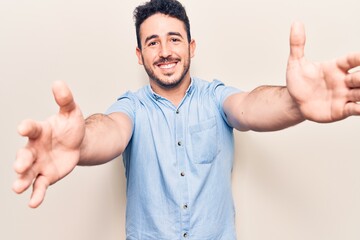 Young hispanic man wearing casual clothes looking at the camera smiling with open arms for hug. cheerful expression embracing happiness.