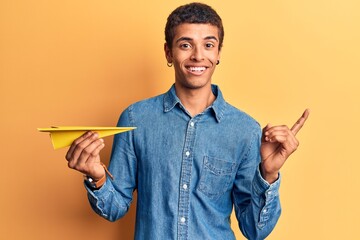 Young african amercian man holding paper airplane smiling happy pointing with hand and finger to the side