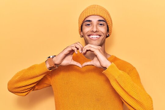 Young african amercian man wearing wool cap smiling in love doing heart symbol shape with hands. romantic concept.