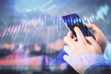 Double exposure of man's hands holding and using a digital device and forex graph drawing. Financial market concept.