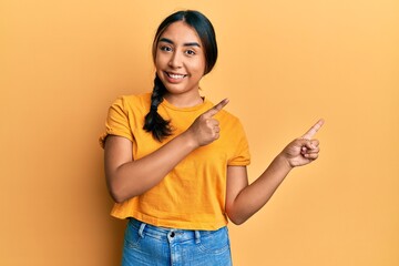 Young latin woman wearing casual clothes smiling and looking at the camera pointing with two hands and fingers to the side.