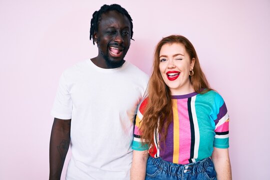 Interracial couple wearing casual clothes winking looking at the camera with sexy expression, cheerful and happy face.