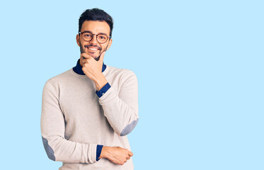 Young handsome hispanic man wearing elegant clothes and glasses looking confident at the camera smiling with crossed arms and hand raised on chin. thinking positive.