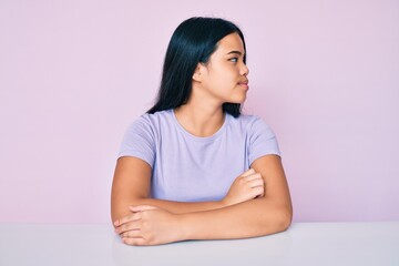 Young beautiful asian girl wearing casual clothes sitting on the table looking to side, relax profile pose with natural face with confident smile.