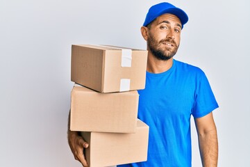 Handsome man with beard wearing courier uniform holding delivery packages looking sleepy and tired, exhausted for fatigue and hangover, lazy eyes in the morning.