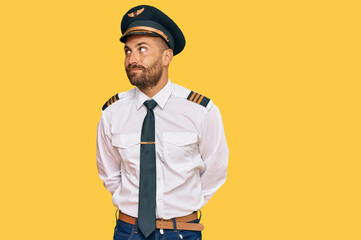 Handsome man with beard wearing airplane pilot uniform smiling looking to the side and staring away thinking.