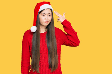 Young chinese woman wearing christmas hat shooting and killing oneself pointing hand and fingers to head like gun, suicide gesture.