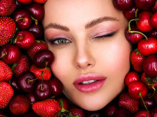 Young, winking girl with bright makeup and a berry background. Happy beautiful caucasian woman.