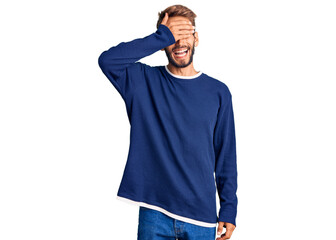 Handsome blond man with beard wearing casual sweater smiling and laughing with hand on face covering eyes for surprise. blind concept.