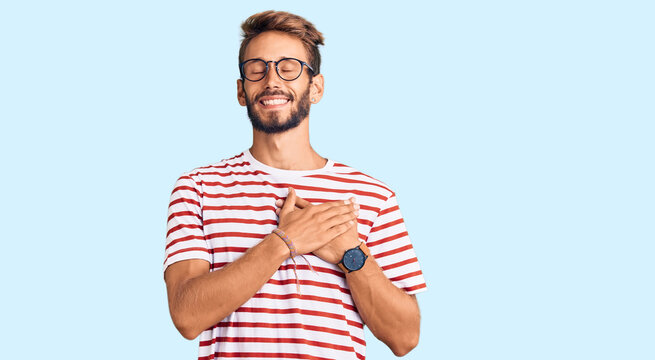 Handsome blond man with beard wearing casual clothes and glasses smiling with hands on chest with closed eyes and grateful gesture on face. health concept.