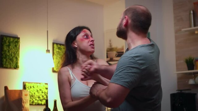 Agresive partner hitting furious wife in the kitchen. Abused terrified beaten woman covered in bruises suffering injury from alcoholic violent brutal aggressive husband screaming.