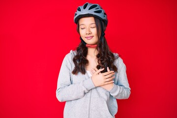 Young beautiful chinese girl wearing bike helmet smiling with hands on chest with closed eyes and grateful gesture on face. health concept.