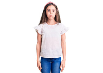 Obraz premium Cute hispanic child girl wearing casual white tshirt puffing cheeks with funny face. mouth inflated with air, crazy expression.