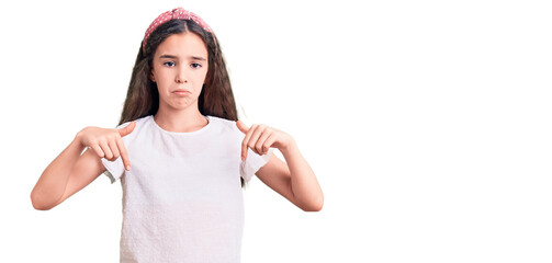 Cute hispanic child girl wearing casual white tshirt pointing down looking sad and upset, indicating direction with fingers, unhappy and depressed.