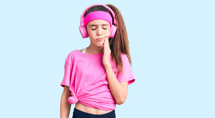 Obraz na płótnie Canvas Cute hispanic child girl wearing gym clothes and using headphones touching mouth with hand with painful expression because of toothache or dental illness on teeth. dentist
