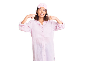 Young beautiful chinese girl wearing sleep mask and pajama smiling cheerful showing and pointing with fingers teeth and mouth. dental health concept.