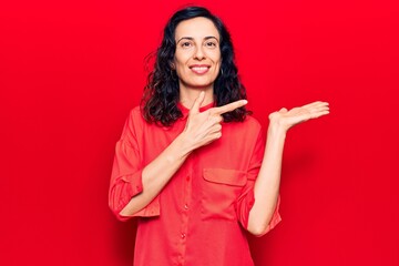 Naklejka premium Young beautiful hispanic woman wearing casual clothes amazed and smiling to the camera while presenting with hand and pointing with finger.