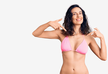 Young beautiful hispanic woman wearing bikini looking confident with smile on face, pointing oneself with fingers proud and happy.