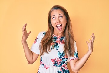 Middle age hispanic woman wearing casual floral dress crazy and mad shouting and yelling with aggressive expression and arms raised. frustration concept.