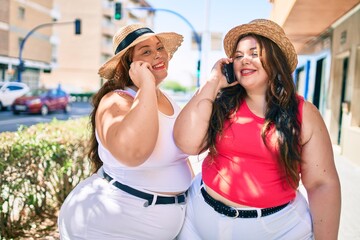 Two plus size overweight sisters twins women speaking on the phone outdoors on a sunny day