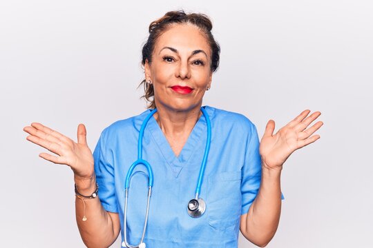 Middle age brunette nurse woman wearing uniform and stethoscope over white background clueless and confused with open arms, no idea and doubtful face.