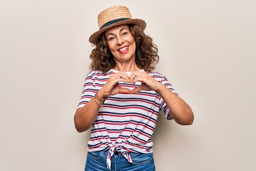 Middle age beautiful woman wearing striped t-shirt and hat over isolated white background smiling in love doing heart symbol shape with hands. Romantic concept.