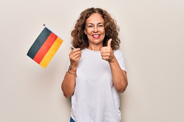 Middle age beautiful patriotic woman holding german flag over isolated white background smiling happy and positive, thumb up doing excellent and approval sign