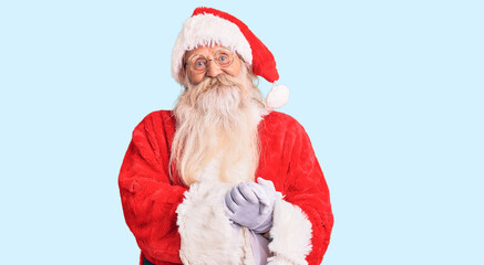 Old senior man with grey hair and long beard wearing traditional santa claus costume with hands together and crossed fingers smiling relaxed and cheerful. success and optimistic