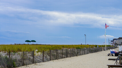 A landscape of beach grass field with fence, USA flag pole and blue sky 