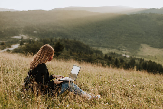 Woman with mask working on laptop on remote location in nature