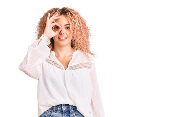 Young blonde woman with curly hair wearing elegant summer shirt doing ok gesture with hand smiling, eye looking through fingers with happy face.