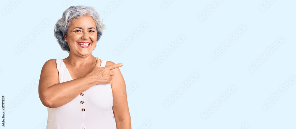 Wall mural Senior woman with gray hair wearing casual clothes cheerful with a smile of face pointing with hand and finger up to the side with happy and natural expression on face