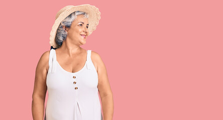 Senior woman with gray hair wearing summer hat and summer clothes looking away to side with smile on face, natural expression. laughing confident.