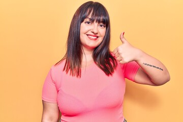 Young plus size woman wearing casual clothes smiling happy and positive, thumb up doing excellent and approval sign