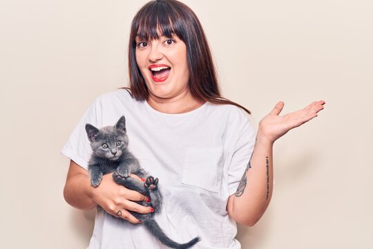 Young plus size woman holding cat celebrating achievement with happy smile and winner expression with raised hand