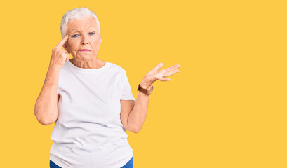 Senior beautiful woman with blue eyes and grey hair wearing casual white tshirt confused and annoyed with open palm showing copy space and pointing finger to forehead. think about it.