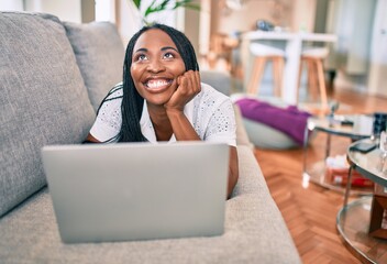 Young african american woman smiling happy working using laptop laying on the sofa at home