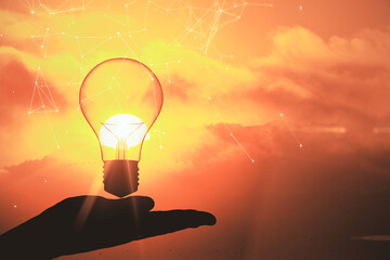 Businessman hand holding glowing lamp on sunrise background.