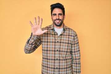 Handsome hispanic man with beard wearing casual clothes showing and pointing up with fingers number five while smiling confident and happy.