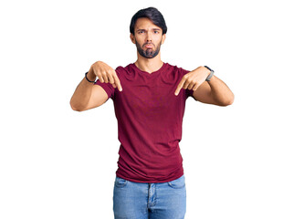 Handsome hispanic man wearing casual clothes pointing down looking sad and upset, indicating direction with fingers, unhappy and depressed.