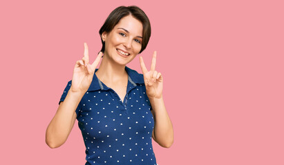 Young brunette woman with short hair wearing casual clothes smiling looking to the camera showing fingers doing victory sign. number two.