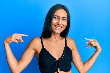 Young brunette woman wearing summer top over blue background looking confident with smile on face,...