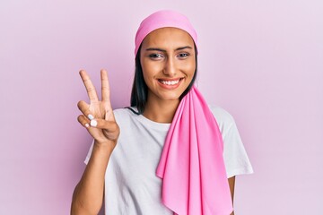 Young brunette woman wearing breast cancer support pink scarf smiling with happy face winking at...
