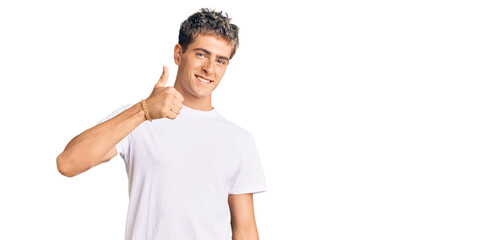 Young handsome man wearing casual white tshirt doing happy thumbs up gesture with hand. approving expression looking at the camera showing success.