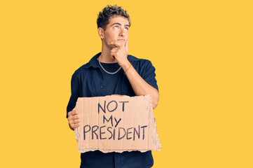 Young handsome man holding not my president protest banner serious face thinking about question...