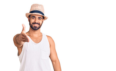 Young hispanic man wearing casual summer hat smiling friendly offering handshake as greeting and welcoming. successful business.