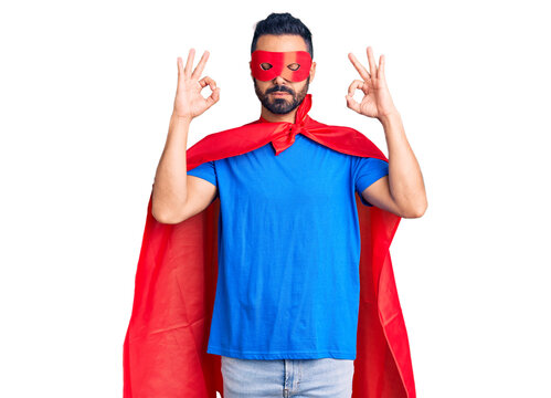 Young hispanic man wearing super hero costume relax and smiling with eyes closed doing meditation gesture with fingers. yoga concept.